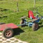 Un kart bleu avec siège rouge et remorque rouge sur pelouse